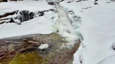Kış harikalar diyarında, karla kaplı kayalar ve sakin bir atmosferi olan çarpıcı bir şelale..