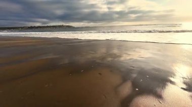 Gün batımındaki çarpıcı bir sahilin manzarası. Parlayan su ve yumuşak dalgalar.