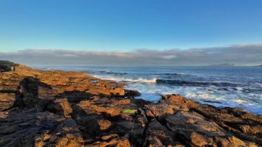 Engebeli, görkemli kayalar ve açık mavi bir gökyüzünün altında hafif dalgaların yer aldığı güzel, sakin bir deniz manzarası.