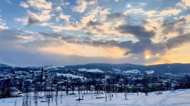 Huzurlu ve sakin bir kış akşamı güzel bir şekilde karlı bir kasabayı canlı, renkli bir gökyüzünün altında sergiliyor.