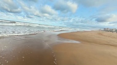 Sakin ve sakin bir sahil. Yumuşak dalgalar, büyüleyici bulutlu gökyüzünün altında yavaşça kıyıları sarıyor.