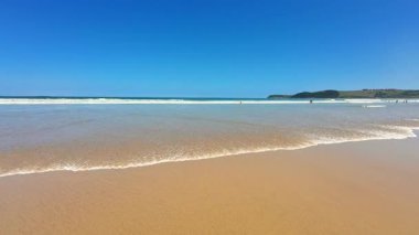 Yumuşak kum, berrak turkuaz su ve inanılmaz derecede canlı mavi gökyüzü içeren güzel ve pitoresk bir sahil sahnesi.