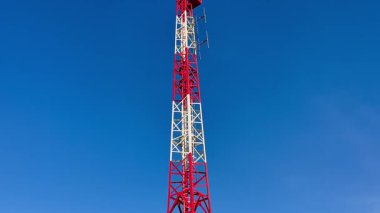 Belirgin kırmızı ve beyaz bölümleri olan yüksek bir iletişim kulesi, açık mavi gökyüzüne güzelce yerleştirilmiş.