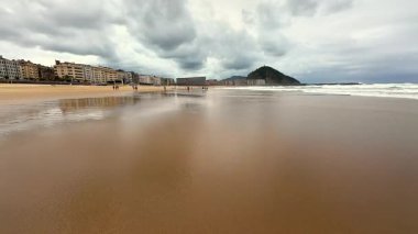 Huzurlu bir sahil sahnesi canlı yansımaları, dramatik fırtınalı gökyüzü, ve arka planda uzak tepeler
