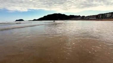 Huzurlu bir sahil manzarası hayal edin. Dalgalar, güzel gökyüzünü ve yakınlardaki manzaralı kıyı tepelerini yansıtıyor.