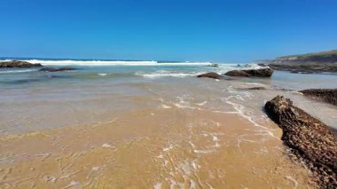 Berrak mavi gökyüzü, yumuşak dalgalar ve sıcak kumlu bir sahile sahip güzel sakin bir sahil manzarası.