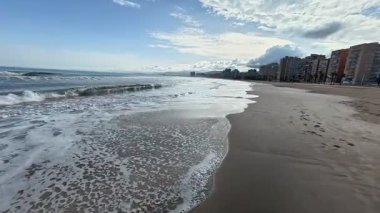 Huzurlu ve huzurlu bir sahil manzarası. Yumuşak dalgalar, altın kum ve yukarıda sakin bir gökyüzü.