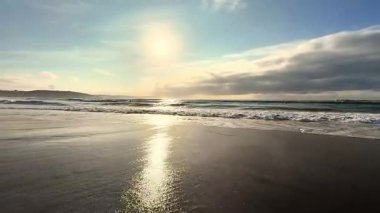 Çarpıcı bir gün batımı, plajın nazik dalgalarına güzel bir şekilde yansıyor. İnanılmaz güzellikler sergiliyor.