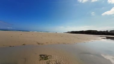 Yumuşak beyaz kum, çarpıcı yansımalar ve yukarıda canlı mavi bir gökyüzünün yer aldığı güzel, sakin bir sahil sahnesi.