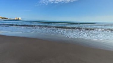 Nefes kesici bir sahil sahnesi yumuşak ve yumuşak kum, nazik ve sakin dalgalar ve canlı, renkli bir gökyüzünü tasvir eder.