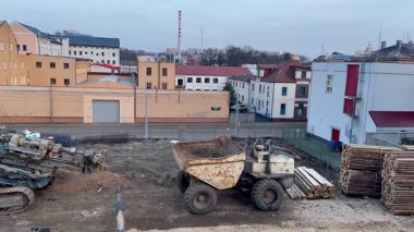 Bu, ağır makinelerin ve çevreleyen binaların bulunduğu hareketli bir inşaat alanının detaylı bir görüntüsü.