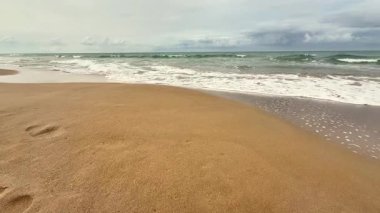 Huzurlu bir sahil sahnesi, sakin dalgalar sergiliyor. Sıcak altın sahilde hafifçe süzülüyor. Rahatlık ve sükuneti davet ediyor.