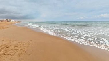 Yumuşak, sıcak kum ve bulutlu bir gökyüzünün altında süzülen yumuşak okyanus dalgalarıyla güzel bir resim sahnesi.