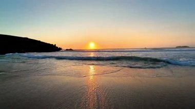 Gün batımının nefes kesici görüntüsü sakin ve durgun sulara güzel bir şekilde yansıyor, sakin bir sahil manzarası yaratıyor.