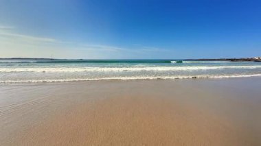 Sakin bir sahil sahnesi kumlu bir sahile ve canlı bir mavi gökyüzüne sahiptir.