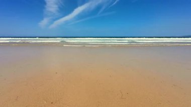 Yumuşak, altın kum, nazik, dalgalı dalgalar ve berrak mavi gökyüzünün yer aldığı şaşırtıcı derecede güzel bir sahil sahnesi.