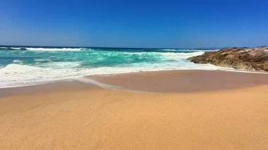 Sakin, berrak mavi bir gökyüzünün altında dalgaların yanında altın kumu aydınlatan nefes kesici bir sahneydi.