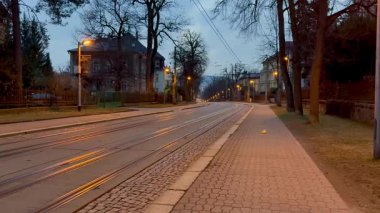 Alacakaranlıkta sakin bir caddenin güzel sakin manzarası, uzak sokak lambalarının altında ışıldayan tramvay rayları