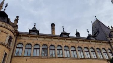 Büyük tarihi yapılar, karmaşık tasarım ve büyük pencereler bulutlu bir gökyüzünün altında güzelce sergilenir.