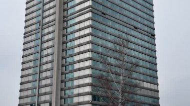 Çağdaş bir ofis kulesi, gri gökyüzüne çarpıcı bir şekilde yerleştirilmiş parlak ve çarpıcı bir cam tasarımı sergiliyor.