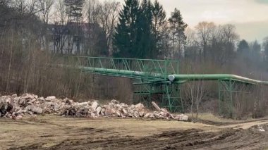 Endüstriyel alan boyunca uzanan uzun yeşil bir konveyör köprüsü ön planda çeşitli enkaz parçalarıyla birlikte...