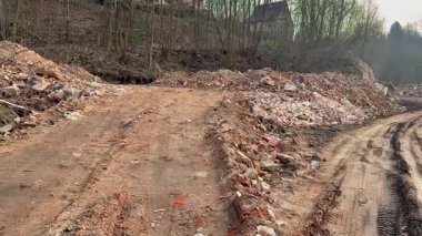 Bir kentsel alan, yeşil, yemyeşil bitki örtüsüyle çevrili toprak bir yola saçılmış inşaat enkazı gösteriyor.