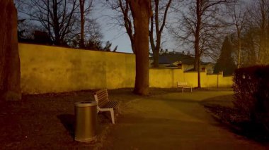 Yumuşak ışıklandırmayla aydınlatılan ve ağaçlarla çevrili büyüleyici bir park yolunu gösteren sakin bir akşam sahnesi.