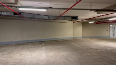 Pürüzsüz beton yüzeyler ve parlak tepe lambaları olan boş bir otoparkın geniş bir görüntüsü