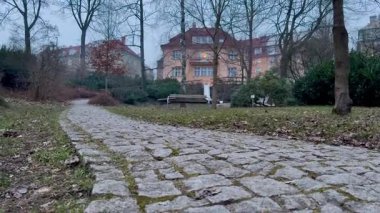 Ağaçlarla kaplı, akşam ışığında büyüleyici bir binaya doğru uzanan huzurlu bir kaldırım taşı yolu..