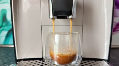 Pürüzsüz bir kahve makinesinden taze demlenmiş bir espresso, ustalıkla temiz bir bardağa dökülüyor.