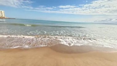 Yumuşak altın kumu, yumuşak dalgaları ve çarpıcı açık mavi gökyüzünü gösteren sakin bir sahil manzarası hayal edin.