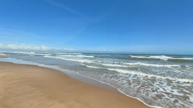 Berrak mavi gökyüzünün altında yumuşak dalgalarla dolu sakin bir sahil. Hoş yaz temaları yakalamak için ideal.