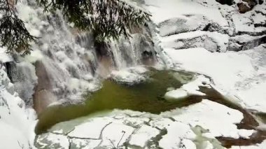 Parlak kar ve buzla çevrili güzel çağlayan bir şelalenin yer aldığı pitoresk bir kış sahnesi hayal edin.