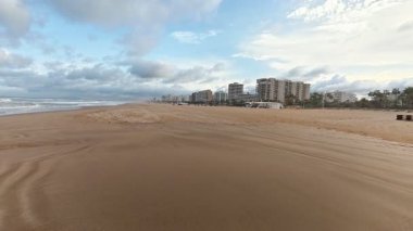 Huzurlu ve huzurlu bir sahil sahnesi yumuşak altın kumlar ve canlı dinamik bir gökyüzü altında kıyı mimarisi sergiliyor.