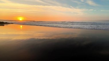 Nefes kesici günbatımı, sakin ve sakin okyanus sularına ve beraberinde nazik dalgalara güzel bir şekilde yansıyor.