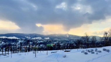 Karla kaplı tepeleri resmeden huzurlu ve sakin bir kış manzarası. Alacakaranlıkta bulutlu güzel bir gökyüzü.