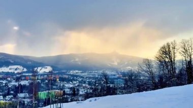 Çok güzel bir kış manzarası var. Karlı dağlar aşağıdaki canlı bir kasabanın tepesinde yükseliyor.