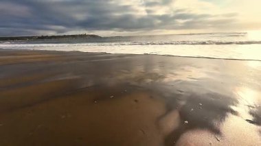 Gün batımındaki çarpıcı bir sahilin manzarası. Parlayan su ve yumuşak dalgalar.