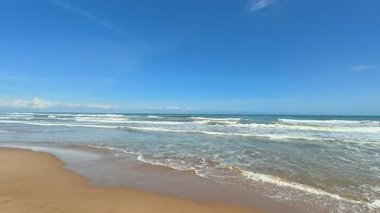 Göz kamaştırıcı ve pitoresk bir plaj sahnesi pırıl pırıl dalgaların mükemmel bir mavi gökyüzünün altında usulca yuvarlandığı