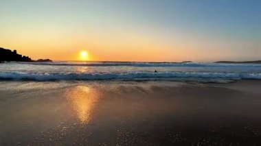 Nefes kesen ve renkli bir gün batımı zarif altın renklerini narin dalgalar arasında, sakin bir sahilde bırakır.