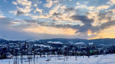 Huzurlu ve sakin bir kış akşamı güzel bir şekilde karlı bir kasabayı canlı, renkli bir gökyüzünün altında sergiliyor.