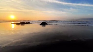 Sakin sahil sularında güzel renklerini yansıtan nefes kesici bir gün batımı. Nazik dalgalar kıyıya vururken.