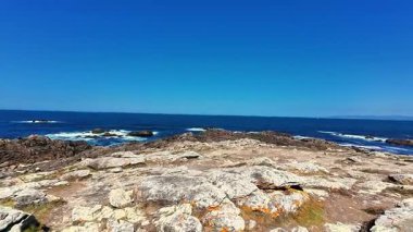 Çarpıcı bir manzara engebeli bir kıyı şeridinin berrak, güzel gökyüzünün altında dingin mavi bir okyanusla birleşmesini gösteriyor.