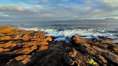 Nefes kesici bir kıyı manzarası dramatik kayalık kıyıları ve bulutlu bir gökyüzünün altında okyanus dalgalarını canlı bir şekilde gösteriyor.
