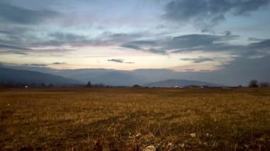 Sakin bir alacakaranlık manzarası engin tarlaları ve uzak tepeleri sergiliyor bulutlu bir akşam gökyüzünün altında zarafetle.