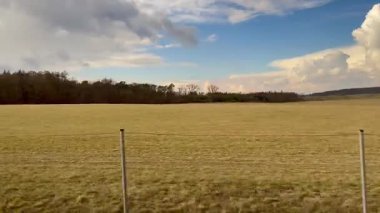 Pofuduk, dağınık bulutlarla benekli, parlak mavi gökyüzünün altında geniş alanlar gösteren huzurlu bir manzara.