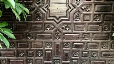 Ayrıntılı bir ahşap duvar paneli, karmaşık geometrik desenler ve gür yeşillik onun güzelliğini arttırır.