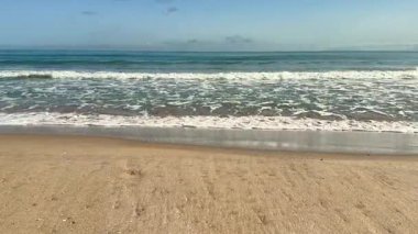 Resmedilmeye değer bir manzara. Yumuşak dalgalar sergiliyor. Güzel kumlu bir kumsalda, berrak mavi bir gökyüzünün altında yavaşça süzülüyor.