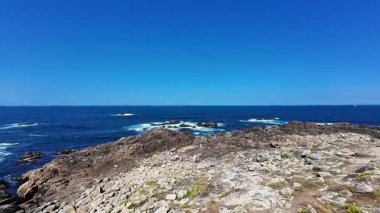 Engebeli kayalık kıyı şeridinin nefes kesici manzarası berrak, güzel mavi gökyüzünün altında engin okyanusla buluşuyor.