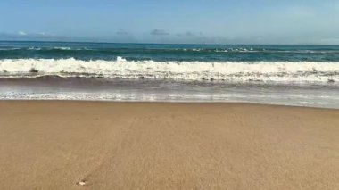 Huzurlu ve sakin bir sahil, parlak beyaz kumların üzerinde, açık mavi gökyüzünün altında yavaşça yuvarlanan altın dalgaları barındırır.